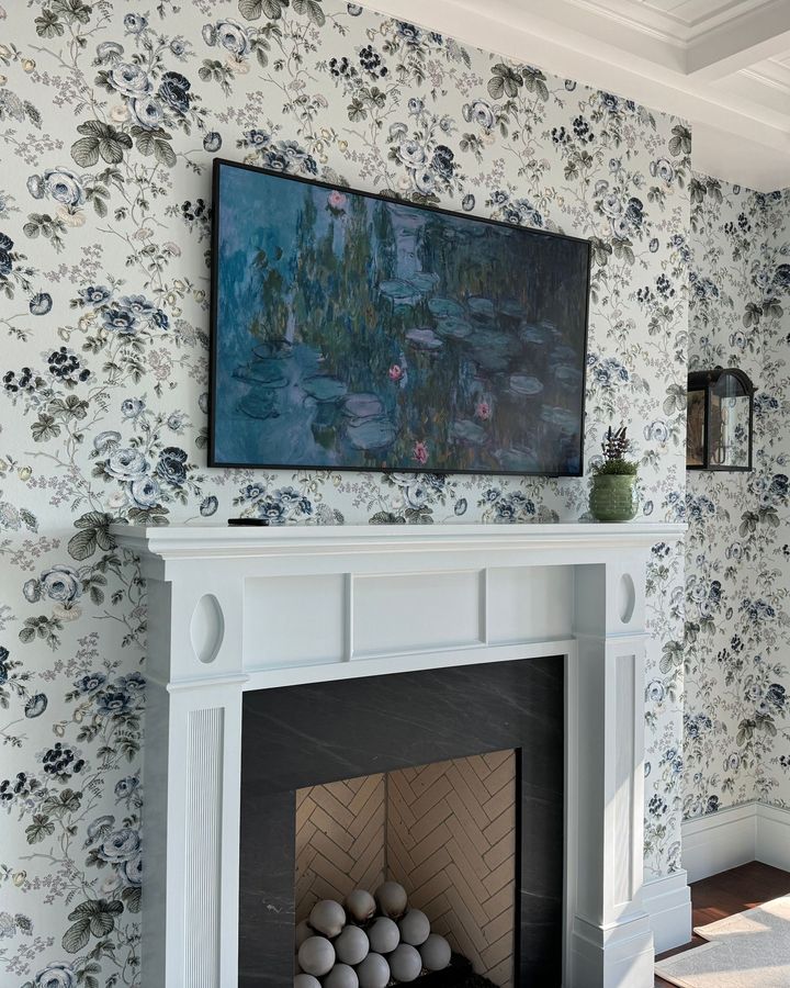 A living room papered in blue-and-white floral wallpaper around a white fireplace mantel