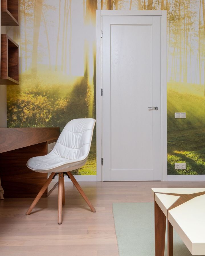 A light home office with a sunlit forest photo mural, a white door, a walnut desk and a white shell chair