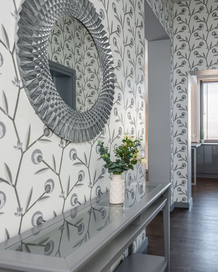 An entry hall papered in grey-on-white stylized vine wallpaper with a sunburst mirror and a console table