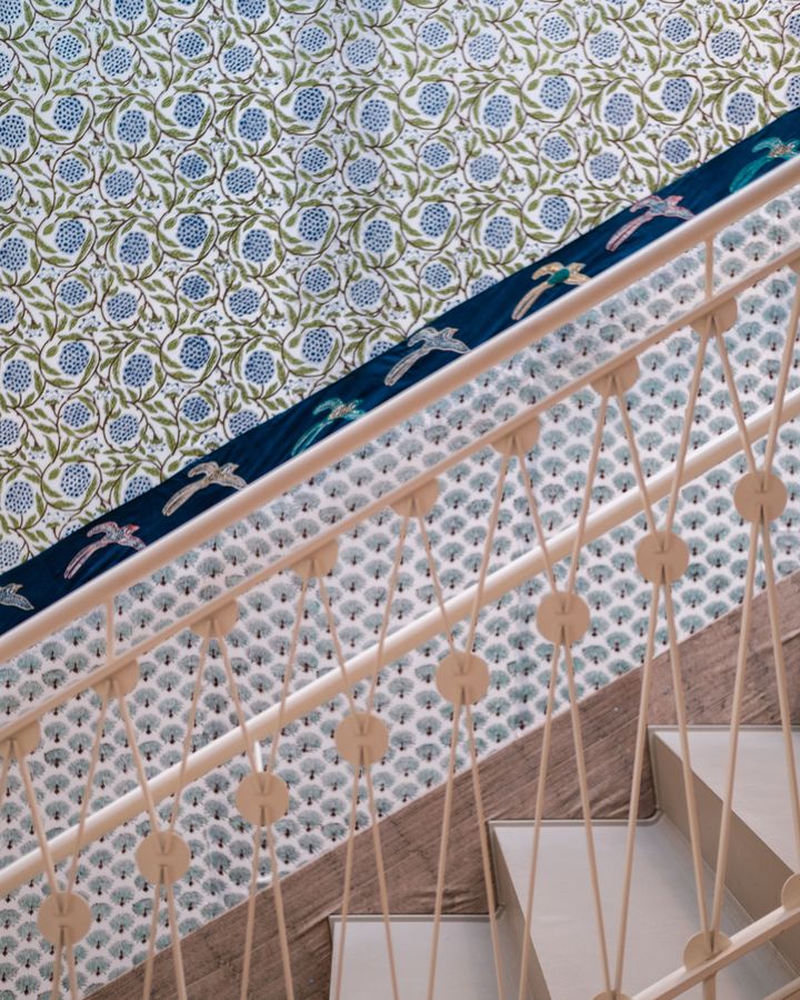 A staircase wall with small-scale blue and green floral wallpaper above a patterned stair stringer and white treads