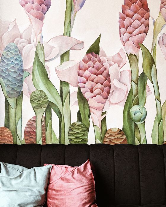 A large watercolor floral mural wallpaper above a black channel-tufted sofa with velvet pillows