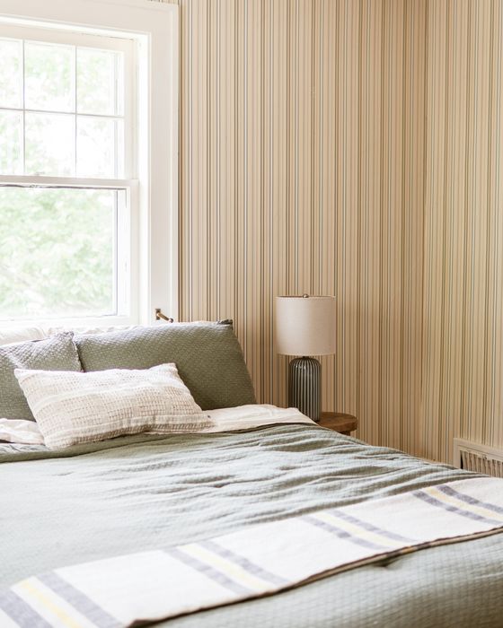 A bright bedroom with fine cream ticking-stripe wallpaper, a white double-hung window and sage bedding