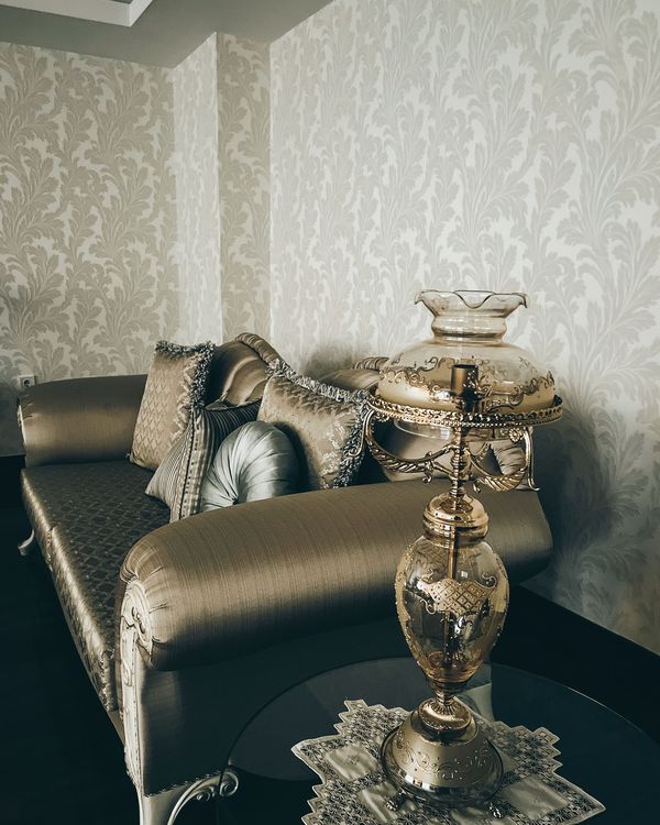 A silver-grey damask wallpaper corner with a satin chaise, tasseled pillows and a crystal lamp